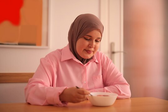 Smiling woman wearing a hijab eats her breakfast