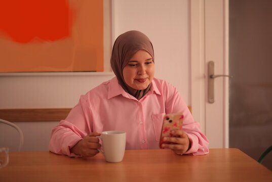 Young woman in hijab enjoys coffee on her phone