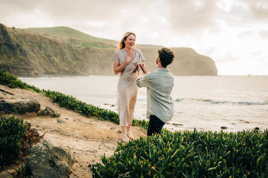 Man proposes to surprised woman on coastal cliff