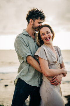 Man lovingly hugging his laughing girlfriend on the beach