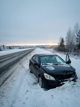 Black sedan car crashed on the side of a snowy road during winter sunset