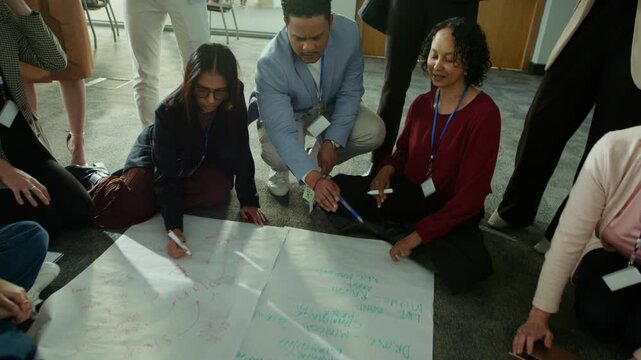 A group of colleagues actively collaborates on a large paper plan during a meeting. They are engaged in thoughtful discussion, sharing ideas and working together effectively on their project.