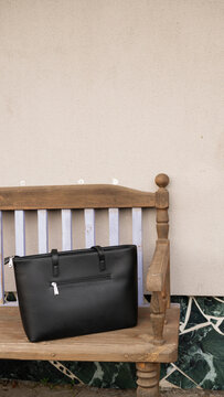 Black leather handbag on wooden bench against cream wall