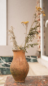 Rustic clay vase with dried wildflowers on marble surface