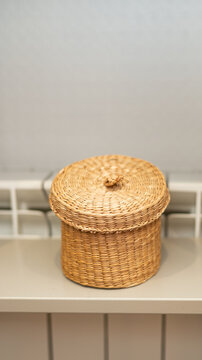 Round woven straw basket with lid on wooden shelf