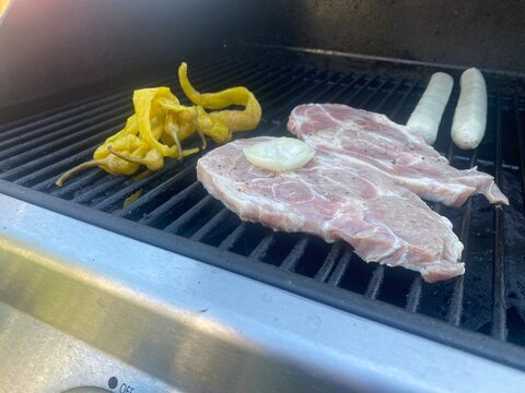 Grill mit marinierten Schweinesteaks, Bratw&uuml;rsten, Paprika und Zwiebeln. Sommerliches BBQ, Grillabend, Barbecue, Outdoor Cooking und herzhafte deutsche K&uuml;che.