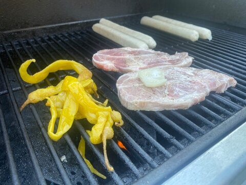 Grill mit marinierten Schweinesteaks, Bratw&uuml;rsten, Paprika und Zwiebeln. Sommerliches BBQ, Grillabend, Barbecue, Outdoor Cooking und herzhafte deutsche K&uuml;che.
