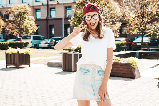 Young beautiful smiling hipster woman in trendy summer clothes. Sexy carefree woman posing on the street background in cap at sunset. Positive model outdoors. Cheerful and happy in sunglasses