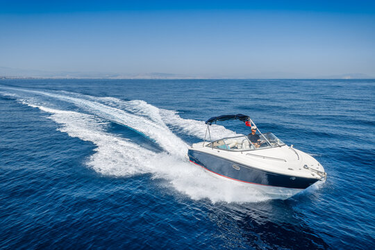 Aerial view of a motorboat cruising with high speed over calm ocean and leaving a trail of surf and waves