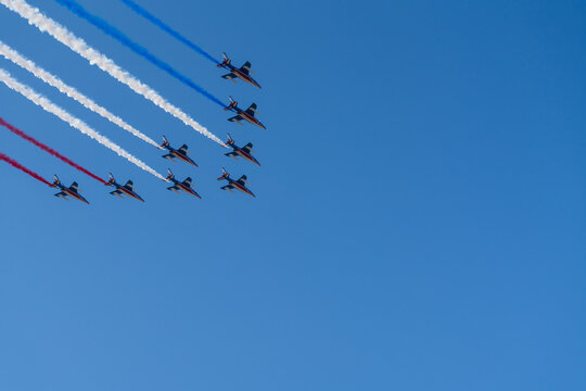 Military jet aircraft formation flying in clear blue sky creating blue white and red smoke trails during air show performance in France