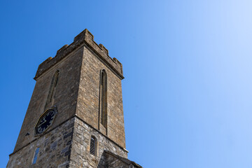 Obraz premium Historic tower of St James’ Church in Yarmouth on the Isle of Wight viewed from below against a clear blue summer sky showcasing traditional English stone architecture and centuries of local heritage
