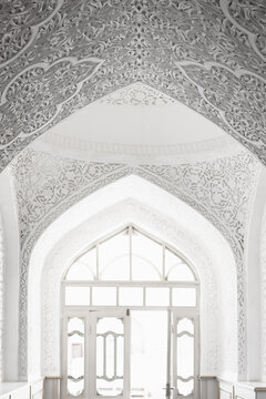 Ornate white interior of Muhammad Amin Khan Madrasa in Khiva with intricate plaster carving and pointed arches. Ideal for travel publications, architecture features, and cultural heritage projects.