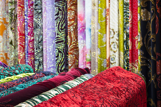 Colorful fabric bolts displayed at an oriental bazaar in Bukhara, Uzbekistan. Glittering textiles with ornate patterns fill the market stall. Ideal for travel, culture, and textile industry content.