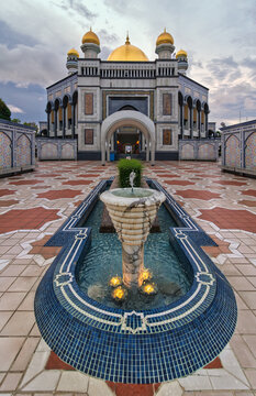 The golden domes of the Jame Asr Hassanil Bolkiah Mosque behind an illuminated water fountain in Bandar Seri Begawan, Brunei, featuring traditional Islamic architecture and intricate tile patterns