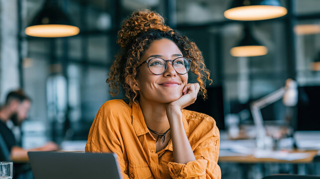 Young woman with glasses working on laptop in office, smiling at desk