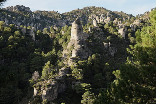 Sunlit limestone rock towers on a green hillside in Els Ports, Spain