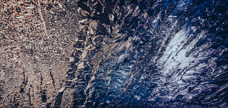 Abstract frost crystals and ice patterns on glass window with warm and cool blue lighting contrast