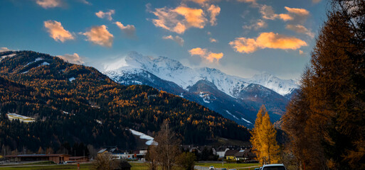 Obraz premium The scenic mountain road in alpine countryside with colorful autumn trees and snow capped peaks with wet asphalt road winding through autumn forest to hallstatt austria at sunset