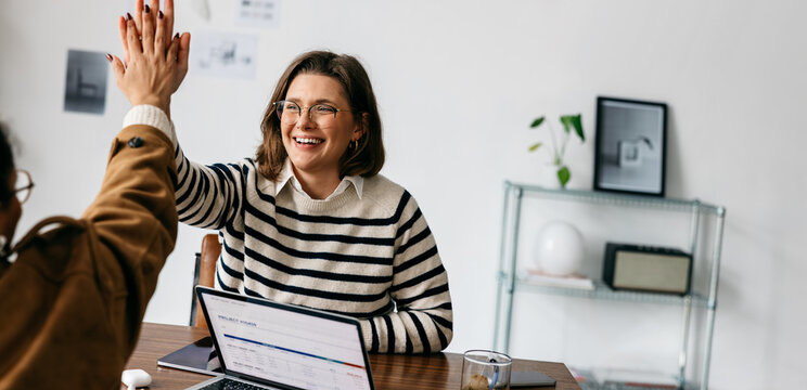 Business people celebrate success with high five during office meeting at laptop desk