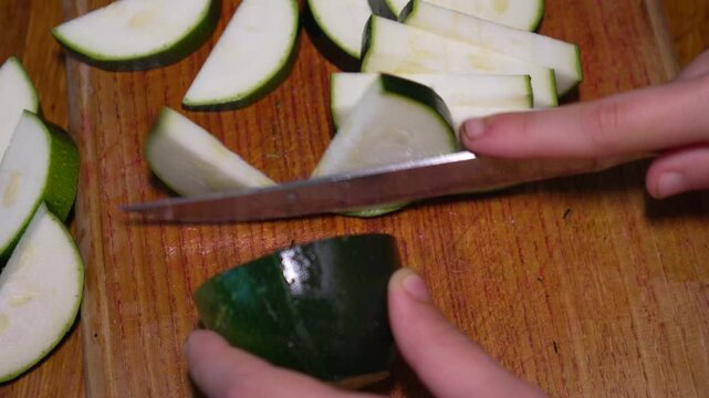 Vegetable preparation, slicing green zucchini on a wooden board. Close up static top-down shot.