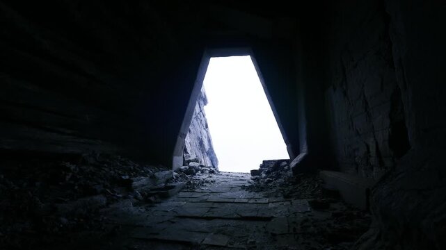 Dim concrete shaft opening to sky, steep interior slope covered with rubble and dust, cold backlight creating deep shadows and high contrast, industrial ruin