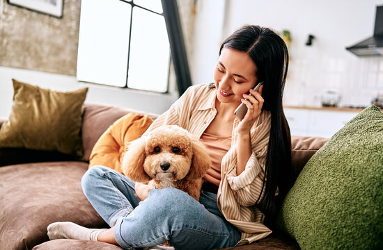 Woman talking on phone with dog on sofa.