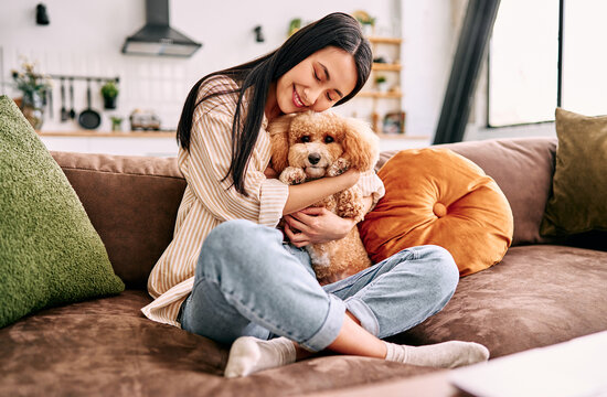 Woman cuddling poodle on sofa at home.