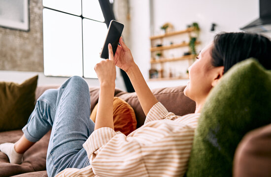 Woman relaxing on sofa and using tablet at home.