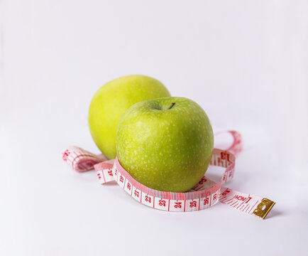 Two fresh green apples with a measuring tape on a clean white surface, representing healthy eating, weight management, nutrition, fitness, and wellness lifestyle concepts