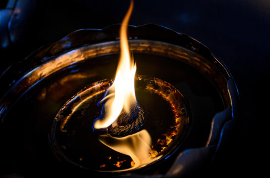 Close-up of a traditional oil lamp with a glowing flame in low light, symbolizing peace, spirituality, meditation, and hope