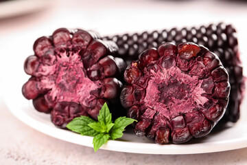 Black sticky rice sweet dessert with purple corn and fresh mint garnish on white plate © BuiThi