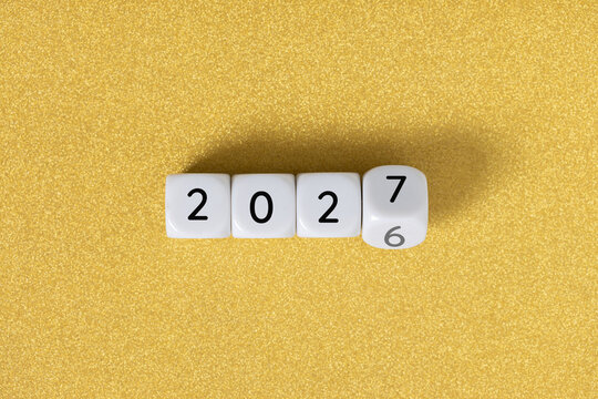 Year 2026 changing to 2027 on dice, glitter festive golden background. New year change concept