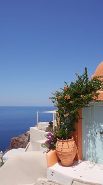 Santorini island, Greece. Colorful architecture with flowers in Oia town. Blue sea and the blue sky at sunny day. Travel and summer vacation concept. Vertical video
