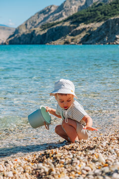 Toddler sitting with bucket on clear lake beach