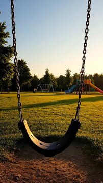Empty swing moving slowly in deserted park at dusk