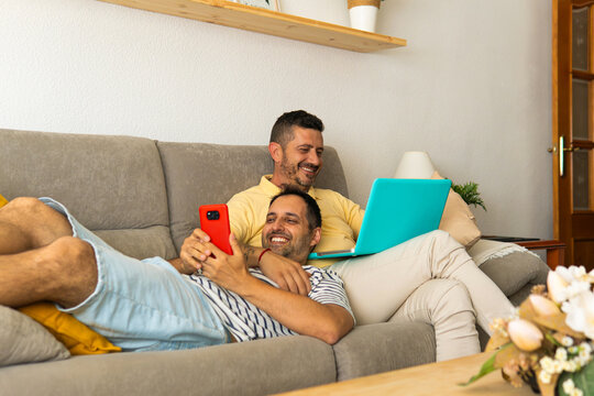 Gay couple relaxing on sofa using technology at home