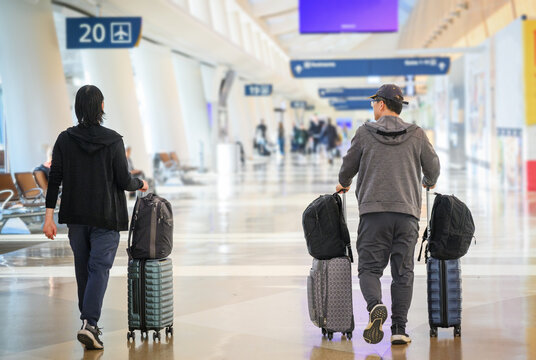 Travellers with roller suitcases and backpacks walking towards the departure gate at the airport. Signs indicating gate numbers. California.