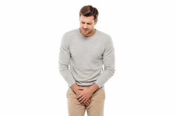 Obraz premium A man in a light grey sweater and tan pants is holding his lower back, suggesting discomfort or pain.