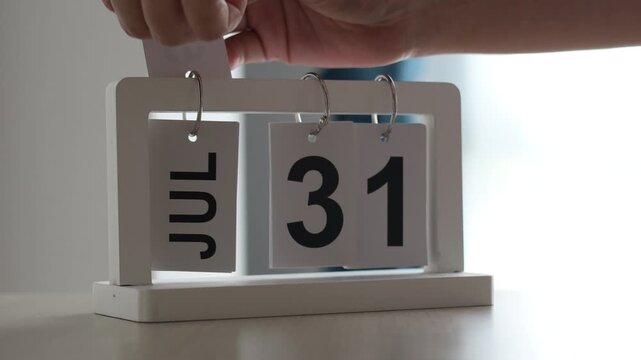 Hand flipping wooden desktop flip calendar from July 31 to August 1, changing month concept, time management and new beginning.