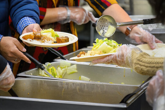 Volunteers in a community kitchen serving hot meals, offering stews, rice dishes and vegetables. California. USA.