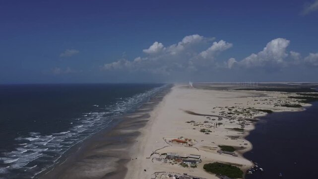 Wide aerial drone perspective showing the narrow sandy strip of Cabur&eacute; surrounded by the ocean, river, and distant wind turbines in Maranh&atilde;o, Brazil.