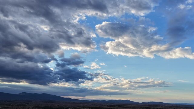4K drone timelapse captures grey and silver clouds over a southwest landscape of mesas and mountains at dusk. The sunset brings changing stormy weather and dramatic light to the high desert terrain.