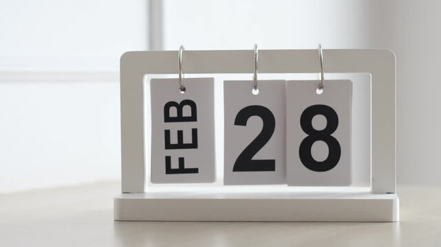Hand flipping wooden desktop calendar from February 28 to March 1, concept of new month, spring season, schedule planning, and time change.