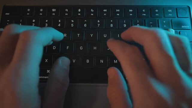 Top view on hands typing on laptop keyboard at night on office or home desk. Man writing programming or coding rapidly pressing on keys and buttons. Hacker working on breaking into secret data server