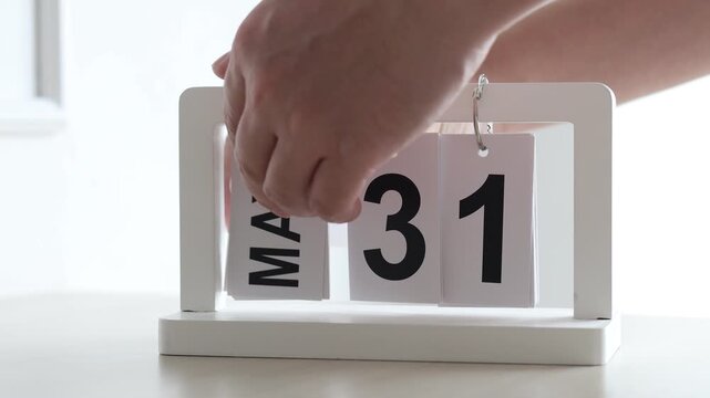 Hand flipping wooden desktop calendar from May 31 to June 1, concept of new month, time change, schedule planning, and start of summer.