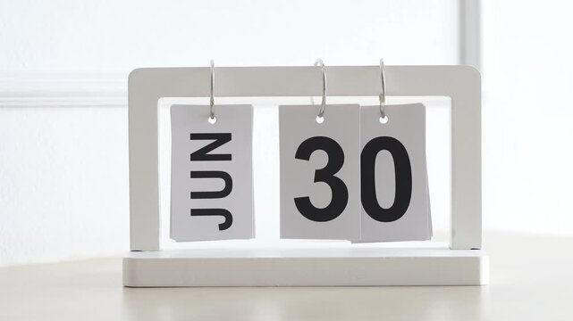 Hand flipping wooden desktop calendar from June 30 to July 1, concept of new month, mid year transition, schedule planning, and time change.