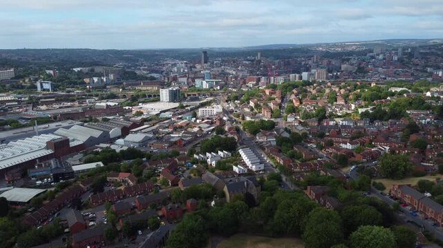 Aerial drone shot with gentle parallax movement overlooking Sheffield city centre from Burngreave on a sunny day with scattered clouds. Urban skyline in South Yorkshire, England.