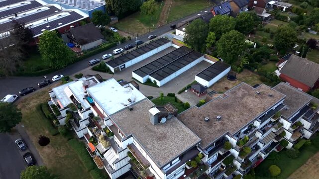 Modern white apartment building with staggered balconies stands beside rooftop solar panels in quiet American neighborhood, parked cars line nearby tree-lined streets. Aerial drone top down