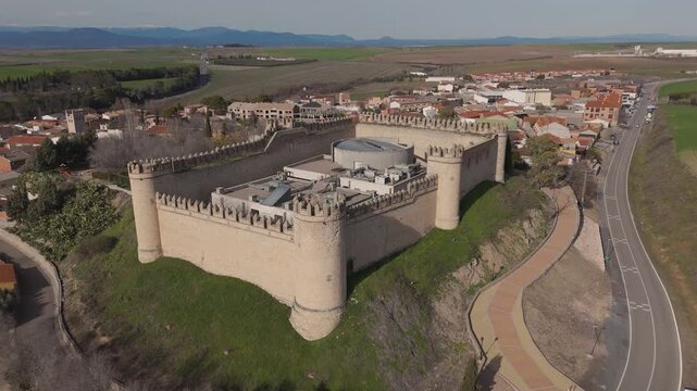 An ascending drone shot over Maqueda Castle with a downward camera movement, revealing the medieval fortress, its contemporary interior structures, the village of Maqueda, and distant mountains