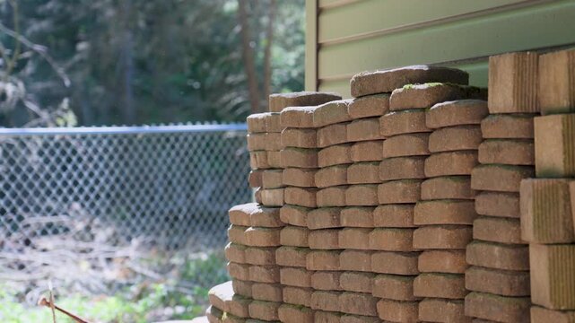 Paver bricks used for landscaping stacked for storage behind a shed.